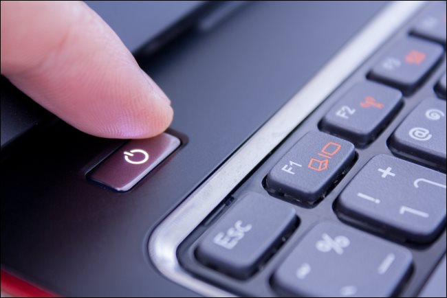 A finger pushing a PC laptop's power button to shut it down.