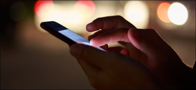 A close-up of hands using a smartphone at night on the street.