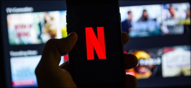 The Netflix logo on a smartphone in front of Netflix on a smart TV.