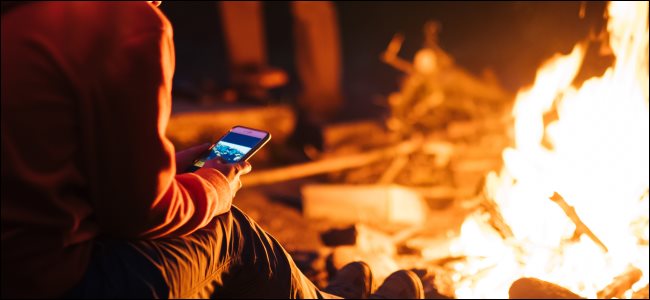 A person using a smartphone in front of a campfire at night.