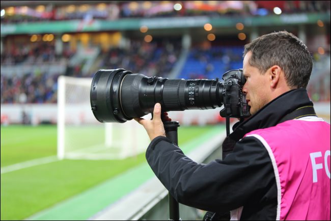 A photographer with a large optical zoom lens at a soccer game.