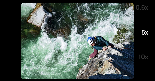 Zoom shot of a man on a rope climbing the rocks next to a rushing river. 